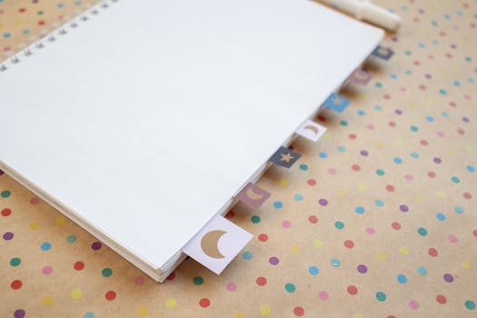A blank spiral notebook with decorative moon tabs on a colorful polka dot background, offering ample copyspace.